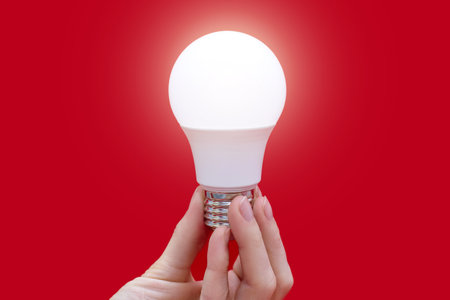 Glowing energy-saving light bulb in hand on a red background. Energy saving and environmental care in everyday life. Conservation and protection of the environmentの写真素材