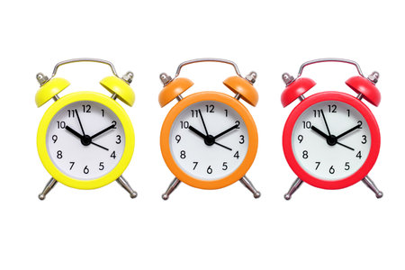 Three multicolored alarm clocks on a white background. Yellow orange and red alarm clock on an isolated white background. Deadline concept in the form of a warming up alarm clockの写真素材