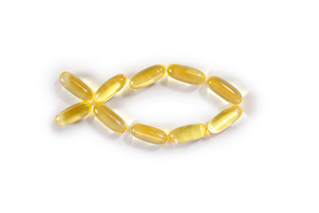 Fish oil capsules in the shape of a fish on a white background in the center. A food supplement for human health that improves the functioning of the cardiovascular system. Bright transparent capsulesの写真素材