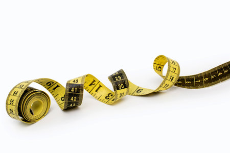 Yellow measuring tape isolated on white background. Tool for measuring length and volume. Yellow-black twisted tape for measuring in the clothing industry or the volume of the human bodyの写真素材