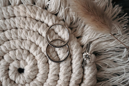 Wedding rings on a fabric background and decorated with a feather. Wedding accessories on the wedding day. Large diamond in the bride's engagement ring. background with wedding ringsの写真素材