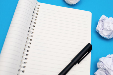 Empty open notepad, pen and crumpled paper wads on a blue background. Free space for text. Top view...
