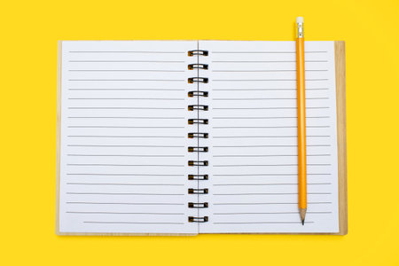 An open notebook with a binding and a pencil on a yellow background. Open notepad with blank sheets in top view. Free space for text. Blank notebook pages ready to be used in designの写真素材