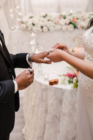 The white bride puts a wedding ring on the finger of the black groom. Multiracial wedding couple. Traditional wedding of ceremony putting on rings close-upの写真素材