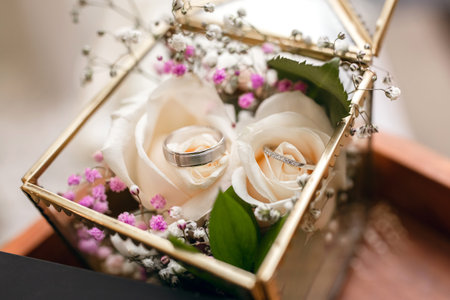 Wedding rings of the bride and groom in a glass box decorated with white roses. Wedding rings at the...