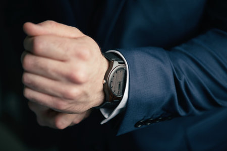 A man in a blue suit and a classic wooden mechanical watch. Close-up man's hands with ecological wooden clock. Mechanical wrist watch made of wood. A man is going to a meeting and puts on a watchの写真素材