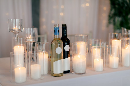 Two bottles of wine decorated with burning candles. A bottle of red and white wine on a table in a restaurant. Party with alcoholic drinksの写真素材