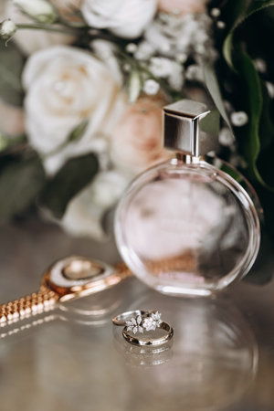 Wedding accessories of the bride in the form of a bouquet of roses, wedding rings with precious stones and perfume. Bridal bouquet of white roses. Wedding rings with precious stones and watchesの写真素材