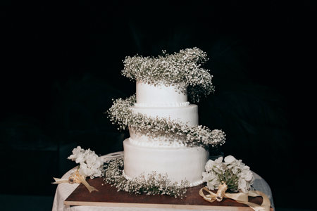 A three-tier wedding cake with white cream decorated with fresh white flowers. A white festive cake stands outside at night. A beautiful white cake is decorated with a spiral of small white flowers.の写真素材