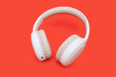 White wireless Bluetooth headphones on a bright orange background. Single wireless headphones for...