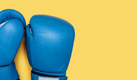 Blue boxing gloves isolated on yellow background close-up with free space for text. A pair of blue leather boxing gloves top view. Boxing accessoriesの写真素材