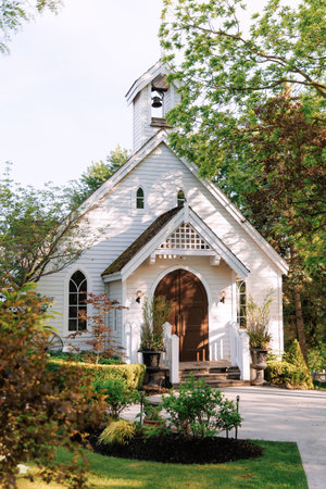 Wooden church with a bell painted white. Beautiful small white church made of wood. Trimmed lawns and trees on the church groundsの写真素材
