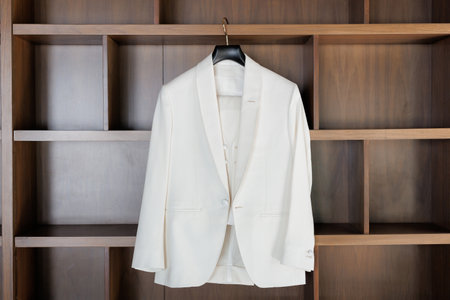 The bride's elegant jacket hangs on a hanger in the room. A white women's jacket hangs on a hanger on a background of wooden shelves. White women's suit jacketの写真素材