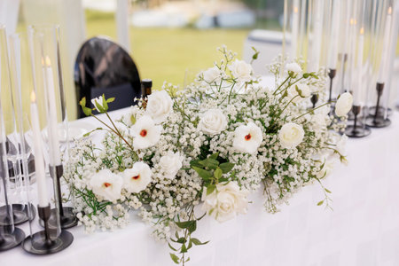 The table of the bride and groom is decorated with flowers and candles. Wedding banquet of newlyweds. Beautiful decor in the form of candles and white flowers on the table of the bride and groomの写真素材