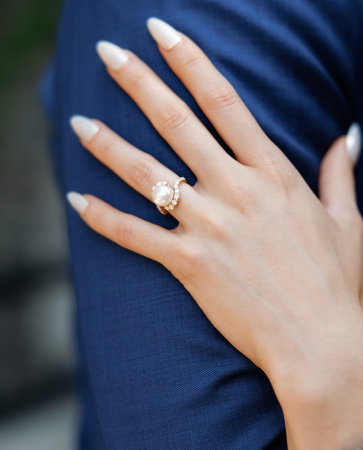 The bride puts her hand on the groom's hand, close-up, cropped photo. The hand of the bride in a wedding ring with a pearl and a manicure holds her hand on the hand of the groom in a blue suitの写真素材