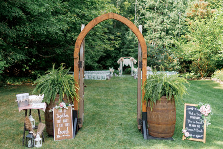 Wooden gates as decor at a wedding ceremony in the forest. An open wooden gate in the middle of a lawn as an entrance to an outdoor wedding ceremony, with a wedding arch and chairs in the backgroundの写真素材