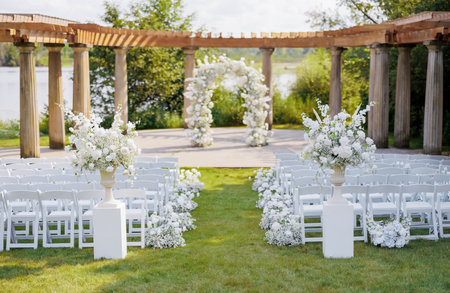 Wedding arch decorated with roses and white chairs for guests against the background of the river. Preparation for the wedding ceremony. Beautiful decor in the form of an arch with white flowersの写真素材
