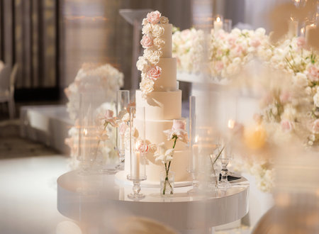 Wedding decorations with flower arrangements, candles and a tiered cake in the center of the restaurant. Luxurious wedding cake with cream roses. Floral installation and lighted candles at the weddingの写真素材
