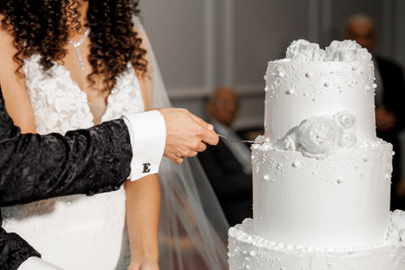 Newlyweds cutting wedding cake during wedding banquet. Hands of bride and groom cutting large white...