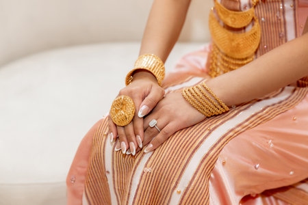 Woman with gold jewelry in ethnic traditional outfit cropped photo. Woman hands in gold bracelets, large ring and wedding ring with diamond dressed in festive national dressの写真素材