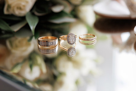 Gold wedding rings and engagement ring with diamond on mirrored table. Bride and groom's wedding...