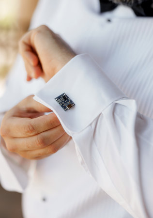 Close-up of a man's hands in a white shirt putting on cufflinks. A man wearing cufflinks shaped like...