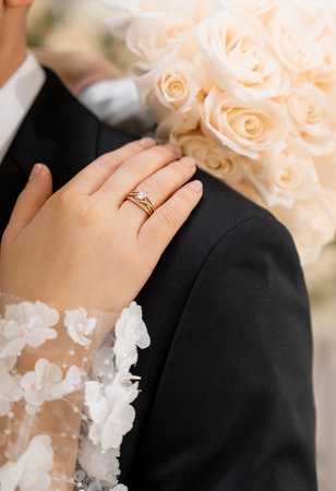Photo a loving couple of bride and groom. Golden wedding ring on the bride's hand on the wedding day. The bride with a wedding bouquet of cream roses put her hand on the groom's shoulder close-upの写真素材