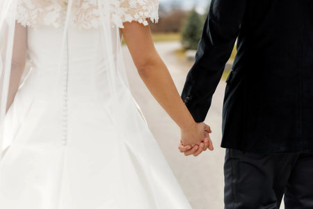 Bride and groom holding hands walking along the road outdoors. Back view of happy wedding couple...