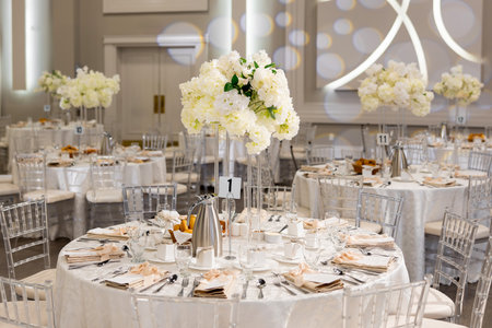 Served tables with white flowers in the center in the large hall create an elegant and festive...
