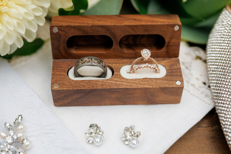 Elegant close-up of wedding rings in a handcrafted wooden box, paired with pearl and crystal...