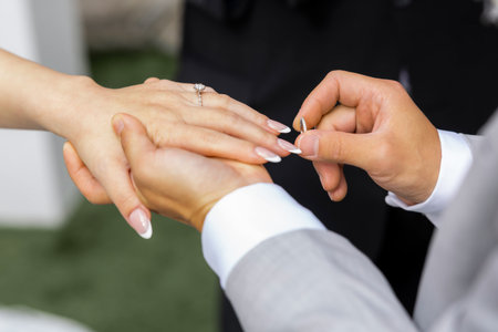 A timeless wedding moment captured in perfection - the groom gently places the ring on the bride's...