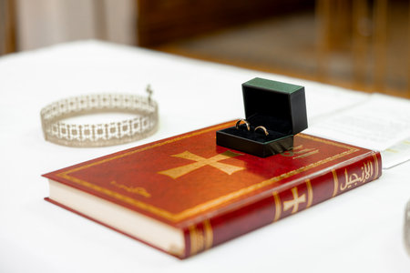 Wedding rings in a black box placed on a red Book of Gospels during a religious ceremony. A silver wedding crown rests nearby, symbolizing tradition, unity, and the sacredness of marriage