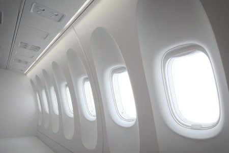 Modern airplane cabin interior with several oval windows allowing bright light to enter, emphasizing a clean and minimalist design without visible passengersの素材