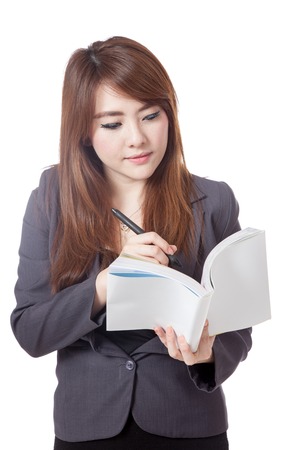 Asian businesswoman is  thinking and writing note in a book isolated on white backgroundの写真素材