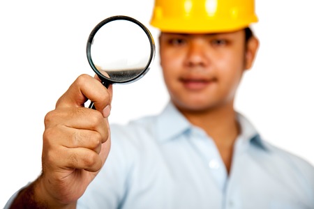 Asian engineer man wear hardhat  hold a magnifying glass focus on the glass isolated の写真素材