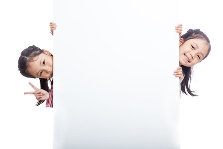 Asian twin sisters  peeking behind empty billboard  isolated on white backgroundの写真素材