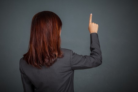 Back of Asian business woman touching the screen with her finger on gray backgroundの写真素材