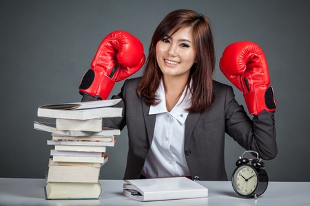 Asian businesswoman ready to fight with boxing glove books and clock on gray backgroundの写真素材