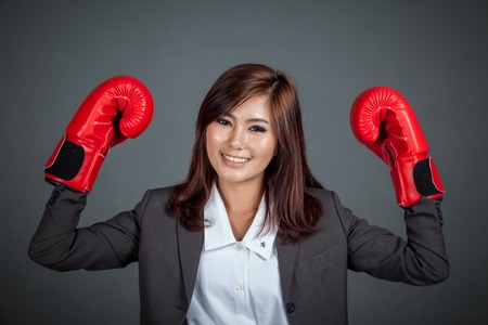 Asian businesswoman with boxing glove show her fists on gray backgroundの写真素材