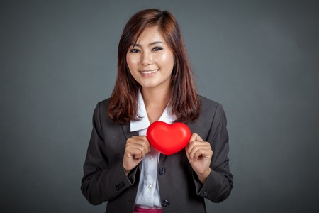 Happy Asian businesswoman show red heart on her chest on gray backgroundの写真素材