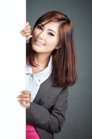 Asian businesswoman stand behind a blank banner and smile on gray backgroundの写真素材
