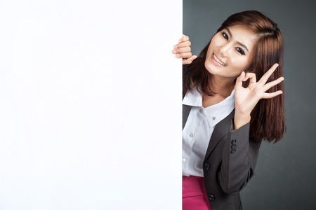 Asian businesswoman stand behind a blank banner show Ok sign on gray backgroundの写真素材