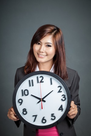 Asian businesswoman hold a clock and smile on gray backgroundの写真素材