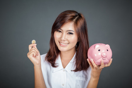 Beautiful Asian girl with a coin and  pink pig money box on gray backgroundの写真素材