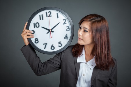 Asian businesswoman show a clock on her shoulder on gray backgroundの写真素材
