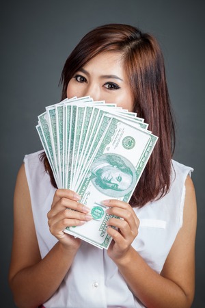 Beautiful Asian girl hold over size 100 dollar bills close her lower face on gray backgroundの写真素材