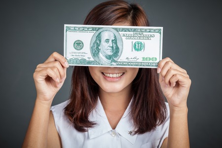 Beautiful Asian girl close her eyes with a 100 dollar bill on gray backgroundの写真素材
