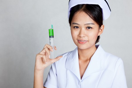 Young Asian nurse hold syringe and smile on gray backgroundの写真素材