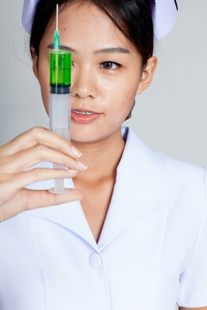 Young Asian nurse look at syringe on gray backgroundの写真素材