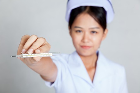 Young Asian nurse show thermometer focus at thermometer on gray background